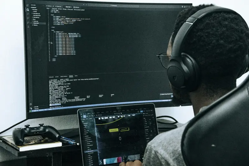 Developer wearing headphones reviewing code on a large monitor