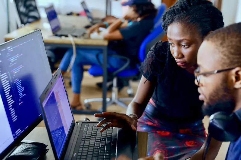 Two software engineers working through code together at a laptop in a shared office